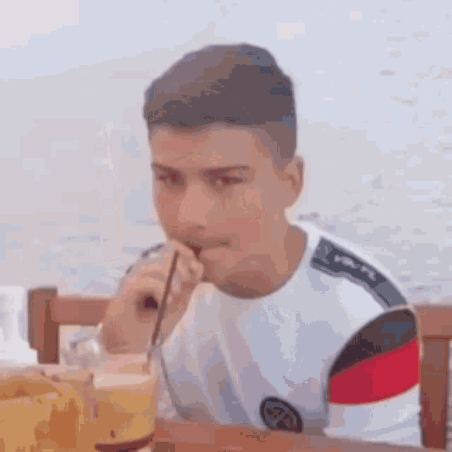 a young man is sitting at a table with a drink in his hand .