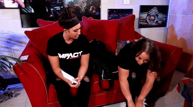two women are sitting on a red couch one is wearing a shirt that says impact