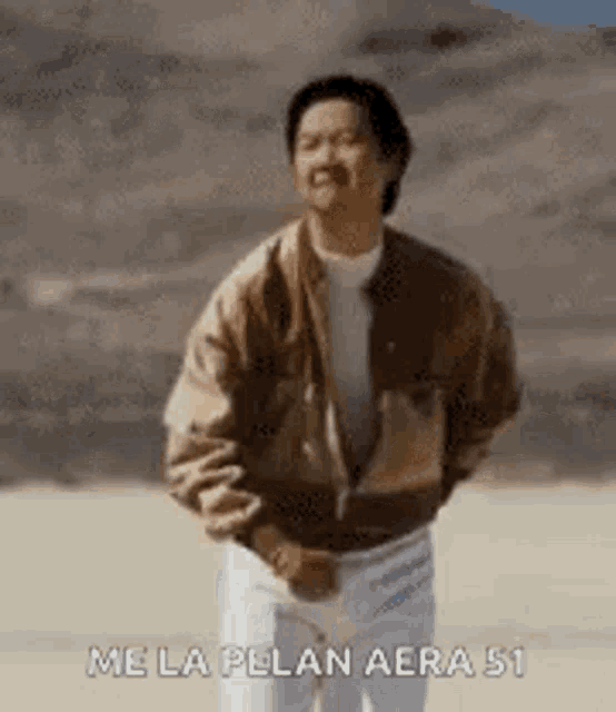 a man in a brown jacket and white pants is standing in a desert .