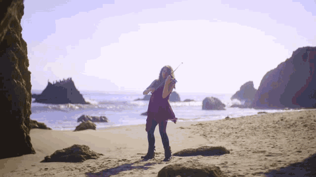 a woman is playing a violin on the beach