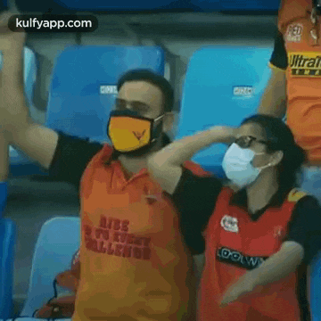 a man wearing a mask and a woman wearing a mask are standing next to each other in a stadium .