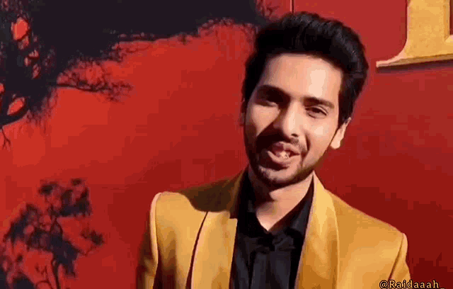 a man in a yellow suit and black shirt is standing in front of a red wall .