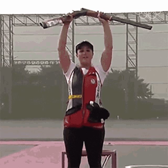 a woman is holding a shotgun over her head while wearing a vest that says ' a ' on it