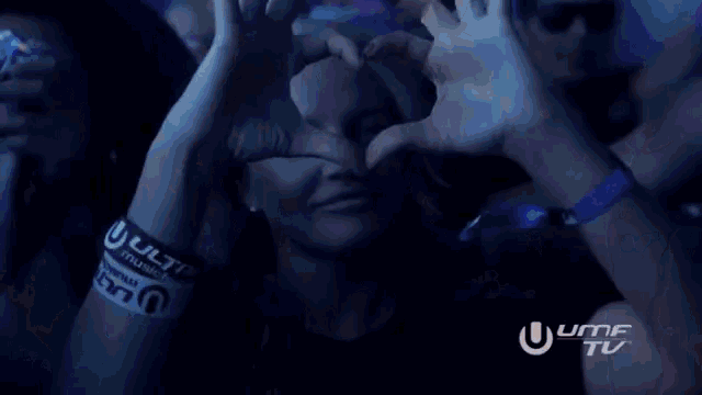 a woman wearing a wristband that says ulti music festival makes a heart shape with her hands