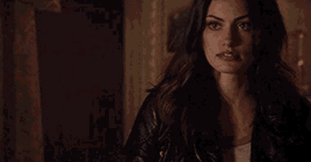 a woman in a leather jacket is standing in a dark room looking at the camera .