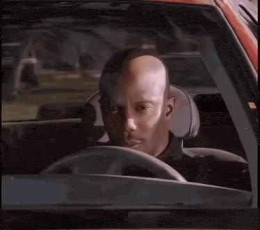 a bald man is sitting in the driver 's seat of a car looking at the camera .