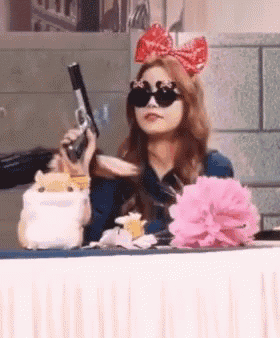 a woman wearing sunglasses is holding a gun in her hand .