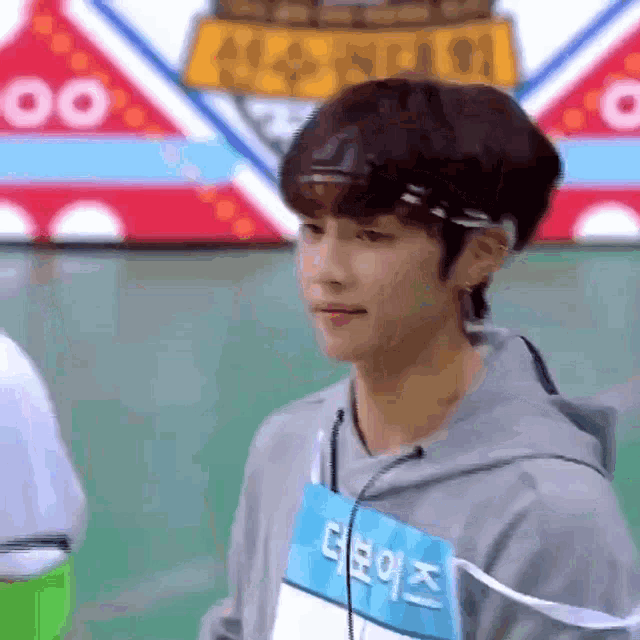 a young man wearing a gray hoodie and a name tag with korean writing on it