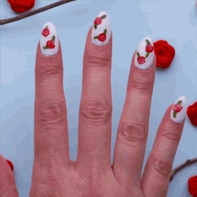 a woman 's nails are painted white with red roses and green leaves