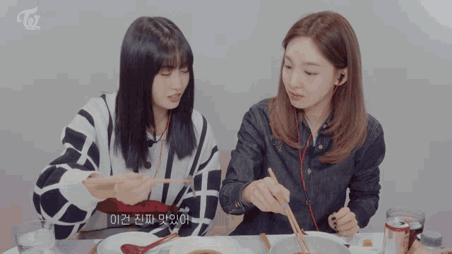 two girls are sitting at a table eating with chopsticks and the word twice is on the bottom of the screen