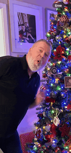 a man standing in front of a decorated christmas tree with a crop logo on the top