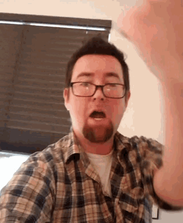 a man wearing glasses and a plaid shirt looks surprised