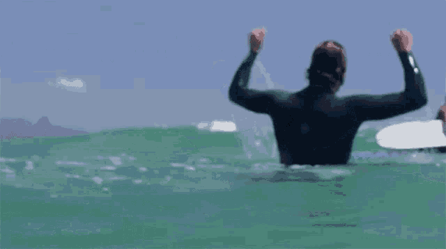 a man in a wetsuit is riding a wave with his arms in the air
