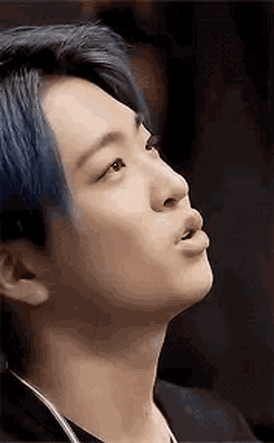 a close up of a man 's face with blue hair and a black jacket .