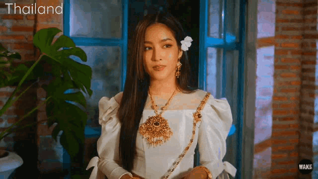 a woman in a white dress with a flower in her hair is standing in front of a window with thailand written on the bottom