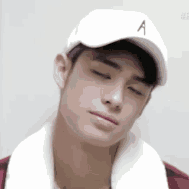 a young man wearing a white baseball cap with the letter a on it is making a funny face with his eyes closed .