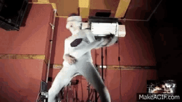 a man in a white suit is standing in front of a red wall holding a machine .