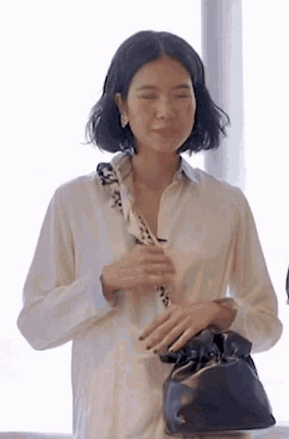 a woman wearing a white shirt and a scarf is holding a black purse .