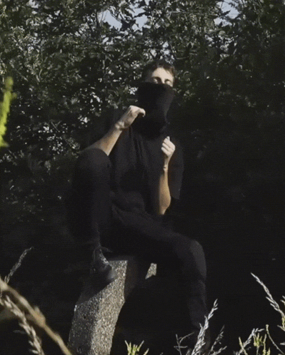 a man wearing a black shirt and black pants is sitting on a rock