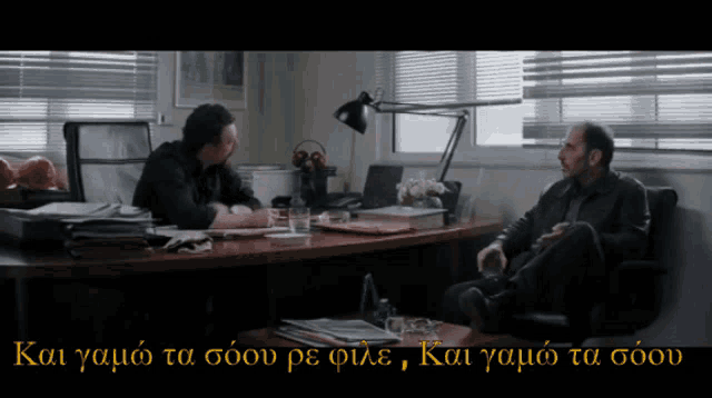 a man sits at a desk with another man in a chair and the words kai yamio ta soov are visible