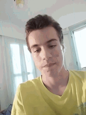 a young man wearing a yellow shirt is looking down at the camera