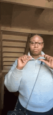 a woman wearing glasses and a light blue sweater is standing in front of stairs .
