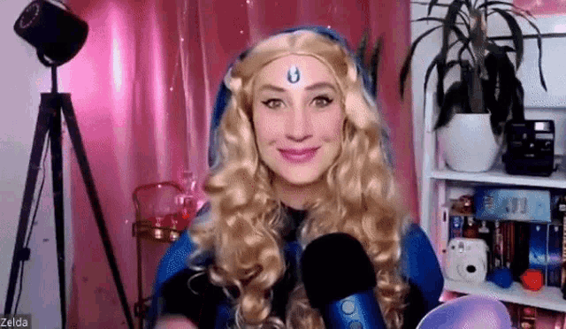 a woman in a zelda costume is holding a microphone in front of a pink curtain .