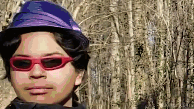 a person wearing red sunglasses and a blue hat is standing in a forest