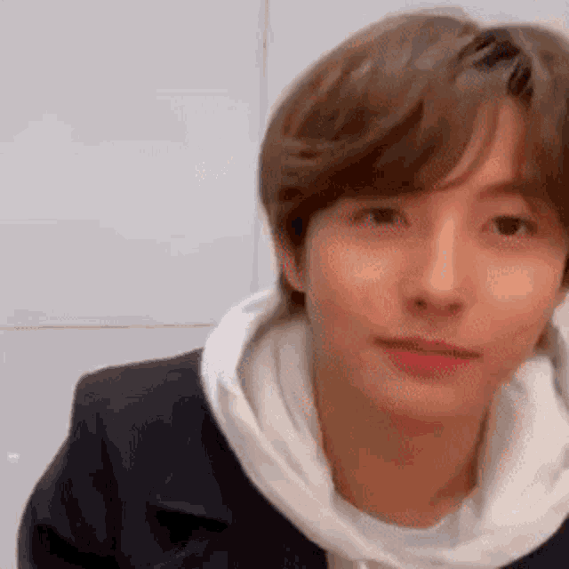 a young man wearing a white hoodie and a black jacket is making a funny face .