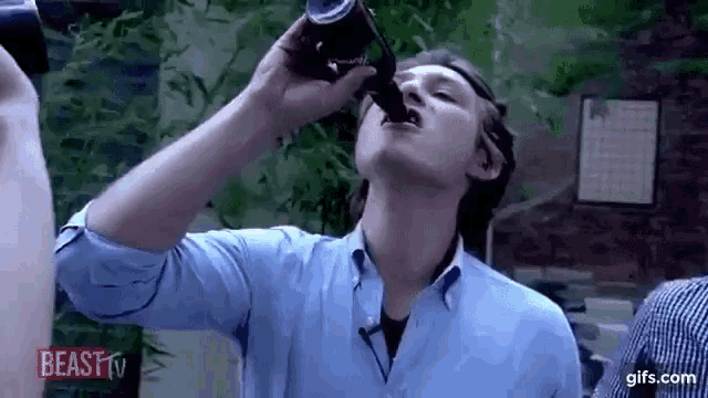 a man in a blue shirt is drinking from a bottle of coke .