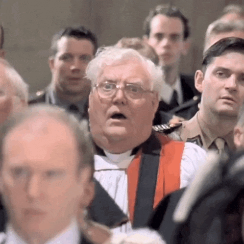 a man with glasses and a red robe is standing in a crowd of people