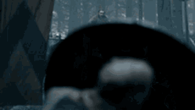 a group of people are standing in a dark forest with a bald man standing in the foreground .
