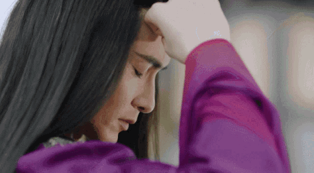 a woman with long black hair is holding her head with her hand .