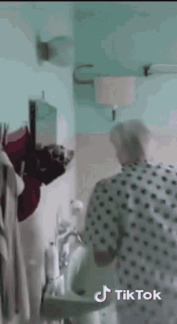 an older woman in a hospital gown is washing her hands in a bathroom sink