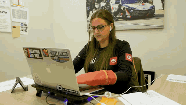 a woman is sitting at a desk with a laptop that has a sticker on it that says ' motorsport for you '