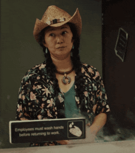 a woman wearing a cowboy hat is standing in front of a sign that says employees must wash hands before returning to work