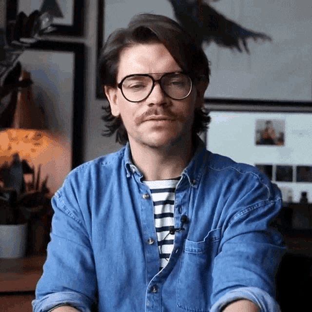 a man wearing glasses and a striped shirt is sitting in front of a computer monitor