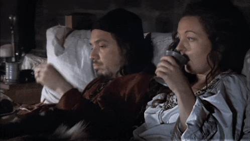 a man and a woman are laying in bed drinking tea