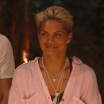 a woman wearing a pink shirt and a necklace is standing in front of a fire .