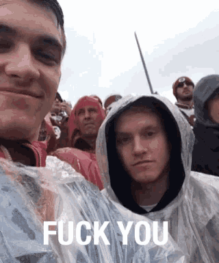 a group of people are standing in the rain and one of them is wearing a plastic raincoat that says " fuck you "