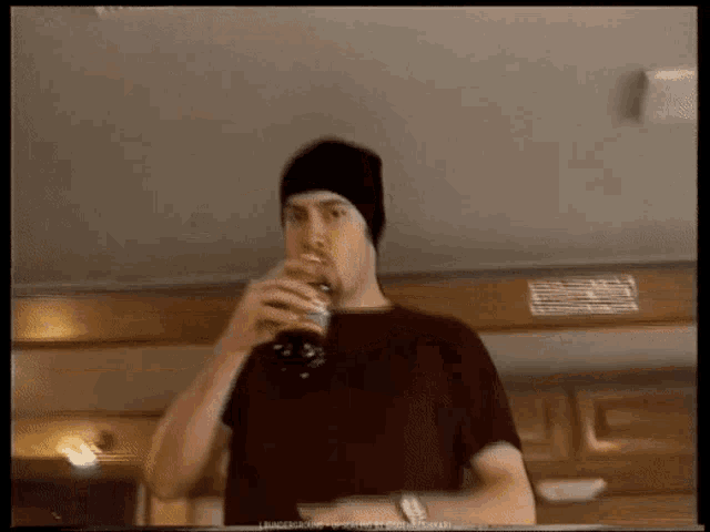 a man wearing a beanie is drinking a bottle of soda
