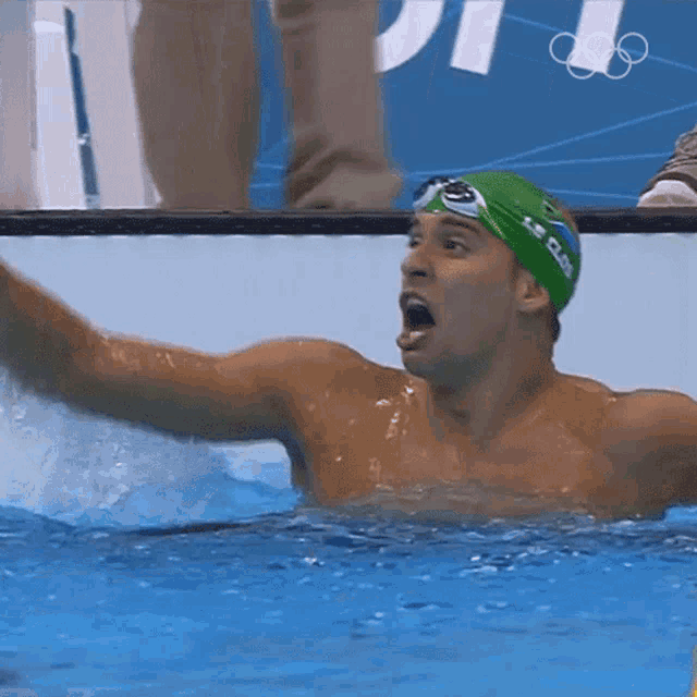 a man wearing a green le club swim cap and goggles is swimming in a pool