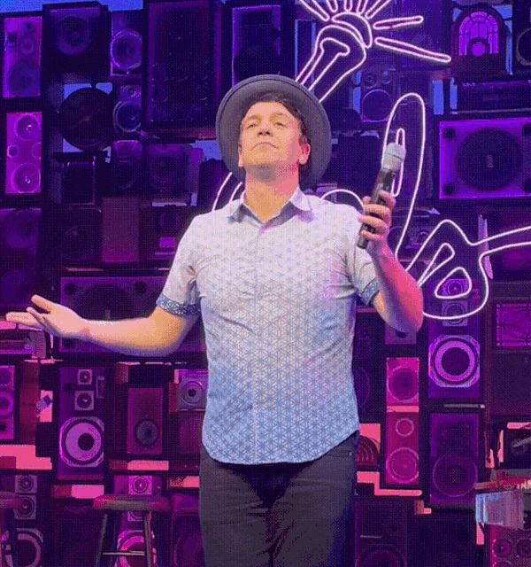 a man in a hat is singing into a microphone in front of a wall of speakers