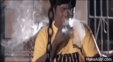 a man in a yellow shirt is smoking a cigarette while sitting on a couch .