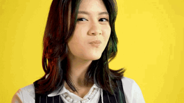 a woman wearing a pearl necklace and a white shirt is making a funny face