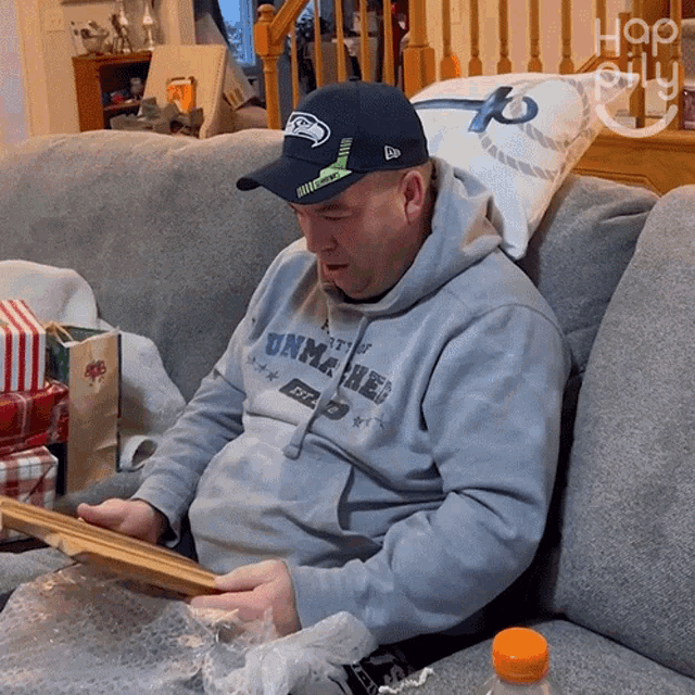 a man wearing a seahawks hat is sitting on a couch looking at a picture