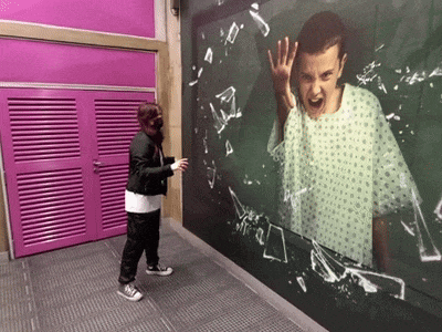 a man in a hospital gown stands in front of a broken glass wall with a picture of eleven on it