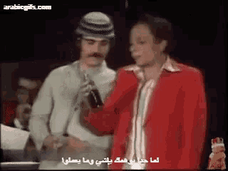 a man in a red jacket is talking into a microphone with another man