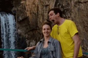 a man in a yellow shirt is standing next to a woman in front of a waterfall