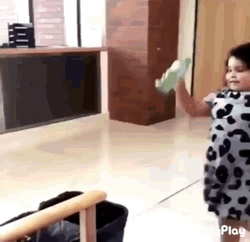 a little girl in a leopard print dress is standing in a room holding a green object .